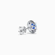 The Nahla 14K White Gold Tanzanite and Diamond Stud Earrings feature round deep blue tanzanite centers, each surrounded by a halo of sparkling white diamonds, beautifully set in 14K white gold against a crisp white background.
