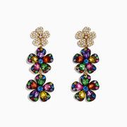 The Watercolors 14K Yellow Gold Multi Sapphire Flower Earrings feature three-tiered sapphire petals outlined in gold, attached to a gold flower stud adorned with sparkling clear crystals.
