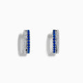 The Royal Bleu 14K White Gold Blue Sapphire and Diamond Huggie Earrings feature a row of blue sapphires bordered by sparkling diamonds on each hoop, shown against a white background.