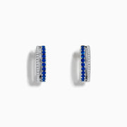 The Royal Bleu 14K White Gold Blue Sapphire and Diamond Huggie Earrings feature a row of blue sapphires bordered by sparkling diamonds on each hoop, shown against a white background.