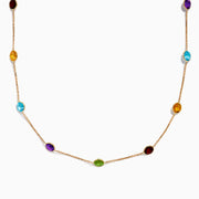 The 14K Rose Gold Multi Color Gemstone Station Necklace features evenly spaced oval gemstones in blue, green, purple, yellow, and red, shown against a white background.
