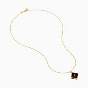 The 14K Yellow Gold Garnet and Diamond Pendant features a four-petal flower-shaped garnet with deep red gemstones outlined in yellow gold and a small clear diamond at the center, shown on a white background.