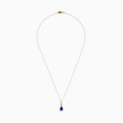 The Nahla 14K Yellow Gold Tanzanite Pendant features a teardrop blue tanzanite surrounded by diamonds and a diamond-accented bail, gleaming at the center of this elegant necklace.
