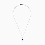 The 14K White Gold Pear Shape Blue Sapphire and Diamond Pendant features a teardrop blue sapphire framed by small clear stones and accented with diamonds set above the main gem.