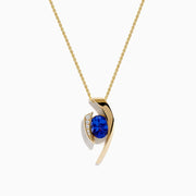 The Nahla Siri 14K Yellow Gold Floating Tanzanite and Diamond Pendant features a vibrant tanzanite gemstone and sparkling diamonds set in a curved gold pendant, displayed on a classic gold chain against a white background.