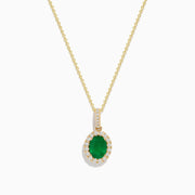 The 14K Yellow Gold Emerald and Diamond Pendant features an oval emerald surrounded by diamonds, suspended from a delicate gold chain and displayed against a white background.