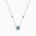 The Lab Grown Blue and White Diamond Halo Necklace in 14K White Gold features a round blue gemstone pendant surrounded by lab grown diamonds, plus two small clear stones set along the chain.