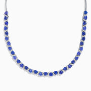 The Nahla Siri 14K White Gold Trillion Cut Tanzanite and Diamond Necklace features alternating deep blue tanzanites and small diamonds set along a 14K white gold chain, elegantly displayed against a white background.