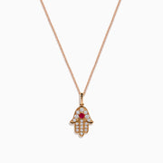 The Ruby Royale 14K Rose Gold Diamond and Ruby Hamsa Pendant features sparkling diamonds and a central ruby, showcased elegantly against a white background.