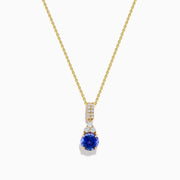 The Nahla 14K Yellow Gold Tanzanite and Diamond Pendant features a round blue tanzanite and white diamonds, set on a yellow gold chain and shown on a white background.