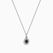 The 14K White Gold Black and White Diamond Halo Pendant showcases an oval black gemstone encircled by sparkling white diamonds, creating a striking contrast against a white background.