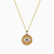 The Novelty 14K Yellow Gold Diamond Evil Eye Disk Pendant features a round design with white and black stones forming the eye, delicately hanging from a gold chain.