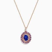 The 14K Rose Gold Pink Sapphire, Tanzanite, and Diamond Double Halo Pendant features an oval-shaped blue gemstone surrounded by pink sapphires, tanzanite, and diamonds on a delicate 14K rose gold chain attached at the top.