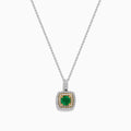 The 14K Two Tone Gold Emerald and Diamond Double Halo Pendant features a central green emerald surrounded by two rows of sparkling diamonds, all suspended from a delicate chain, showcased on a white background.
