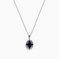 A 14K white gold Sapphire and Diamond Vintage Halo Pendant, featuring a large oval blue sapphire surrounded by smaller diamonds in a floral pattern, is displayed on a white background.