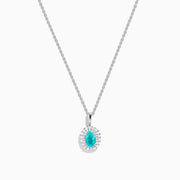 An 18K White Gold Paraiba and Diamond Pendant with an oval Paraiba gemstone and a halo of diamonds hangs from a delicate chain, shown against a plain white background.