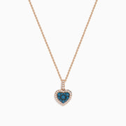 The Bella Bleu 14K Rose Gold Blue and White Diamond Heart Pendant features a heart-shaped design with blue diamonds at the center, bordered by white diamonds, hanging vertically on a rose gold chain against a white background.