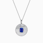 The 14K White Gold Tanzanite and Diamond Fluted Circle Pendant features a round diamond-accented design with a radiant motif and a central emerald-cut blue tanzanite stone.