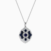 The 14K White Gold Sapphire and Diamond Vintage Pendant features deep blue sapphires and sparkling diamonds in a geometric design, suspended from a delicate white gold chain, all displayed on a white background.