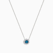 The Bella Bleu 14K White Gold Pendant showcases a round blue and white diamond centerpiece, accented by a halo of 0.60 TCW diamonds, elegantly presented on a white background.