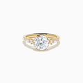 The Star Lab Grown Diamond Moderne Ring in 18K Yellow Gold features a large round lab diamond center, two smaller round diamonds, and baguette-cut side diamonds, shown on a white background.