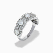 The 18K White Gold Diamond Round Halo Band Ring showcases three central round diamonds, each with a diamond halo, and features rectangular diamond accents on the sides for added brilliance.