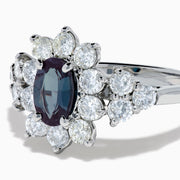 A Platinum GIA Certified Alexandrite and Diamond Starburst Halo Ring, featuring an oval dark blue-green central Alexandrite and sparkling diamond accents, displayed on a white background.