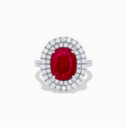 The 18K White Gold Ruby and Diamond Double Halo Ring features an oval ruby encircled by two rows of round white diamonds, set in a sleek 18K white gold band and displayed on a white background.