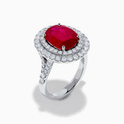 The 18K White Gold Ruby and Diamond Double Halo Ring features an oval ruby encircled by two rows of round white diamonds, set in a sleek 18K white gold band and displayed on a white background.