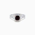 The 18K White Gold GIA Certified Alexandrite and Diamond Ring showcases a cushion-cut Alexandrite surrounded by white diamonds. Its split band is adorned with diamonds, adding elegance, and the ring is displayed against a plain white background.