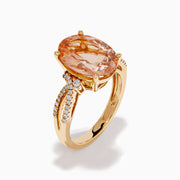 The 14K Rose Gold Morganite and Diamond Twist Band Ring features an oval peach morganite center stone with rows of white diamonds on a unique twist band, shown against a white background.