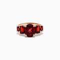 The 14K Rose Gold Multi Shape Garnet and Diamond Hidden Halo Ring showcases a central oval deep red garnet, accented by smaller rectangular and oval garnets on each side, all set in polished rose gold.