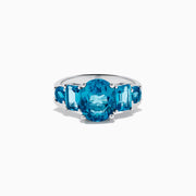 The 14K White Gold Multi Shape Blue Topaz and Diamond Hidden Halo Ring showcases a bold oval blue topaz center, accented by rectangular and round blue stones on each side, all set in a polished band with a subtle diamond hidden halo.