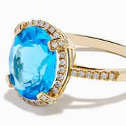 The Ocean Bleu 14K Yellow Gold Blue Topaz Ring showcases a large oval center blue topaz, embraced by a diamond halo and additional diamonds adorning the band.