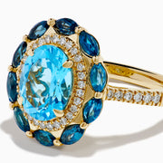 The Ocean Bleu 14K Yellow Gold Blue Topaz and Diamond Ring showcases a large oval blue topaz center, haloed by clear diamonds and marquise deep blue stones, all set on a textured yellow gold band.