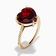 The Bordeaux 14K Yellow Gold Garnet and Diamond Heart Ring features a large heart-shaped deep red garnet at the center with small diamonds on the band, shown against a white background.