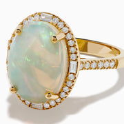 The 14K Yellow Gold Opal and Diamond Halo Cocktail Ring showcases an oval opal centerpiece encircled by a shimmering diamond halo, set against a white background.