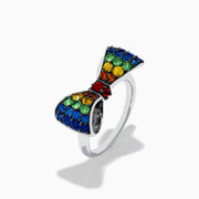 The Safari 925 Sterling Silver Multi Color Sapphire Bow Ring features red, yellow, green, and blue sapphires arranged symmetrically in a bow design against a white background.