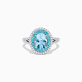 The Aquarius 14K White Gold Aquamarine, Paraiba, and Diamond Ring features an oval aquamarine center stone encircled by two halos of sparkling blue Paraiba and clear diamonds, displayed on a plain white background.