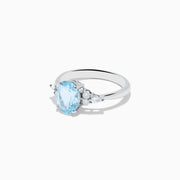 The Aquarius 14K White Gold Aquamarine and Diamond Ring showcases an oval light blue aquamarine center stone, accented by three small round diamonds on each side, set against a plain white background.