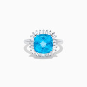 The Ocean Bleu 14K White Gold Blue Topaz and Diamond Halo Ring features a large cushion-cut blue topaz center stone, surrounded by a sparkling halo of baguette-shaped diamonds, all set in elegant white gold.