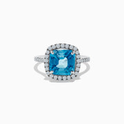 The 14K White Gold Blue Zircon and Diamond Ring showcases a large cushion-cut blue zircon center, surrounded by a halo of small round diamonds on the setting and band, set against a white background.