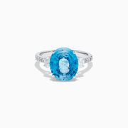 The 14K White Gold Blue Zircon and Diamond 3 Stone Ring features a large oval blue zircon center stone with diamonds on each side, shown on a white background.