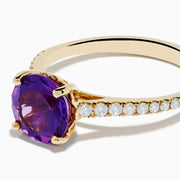 The 14K Yellow Gold Amethyst and Diamond Ring showcases a large round amethyst center accented with small white diamonds along the band, displayed on a white background.