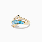 The Ocean Bleu 14K Yellow Gold Blue Topaz and Diamond Bypass Ring features sparkling white diamonds on one side and a row of rectangular blue topaz stones on the other in an elegant bypass design.