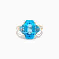 The Ocean Bleu 14K Yellow Gold Blue Topaz Ring showcases a large emerald-cut blue topaz, accented by two smaller matching stones, all set on a sleek, elegant gold band.