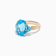 The Ocean Bleu 14K Yellow Gold Blue Topaz Ring showcases a large emerald-cut blue topaz, accented by two smaller matching stones, all set on a sleek, elegant gold band.