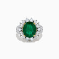 The 18K Two-Tone Gold Emerald, Yellow and White Diamond Ring features a striking oval green emerald surrounded by white diamonds, set in a gold and silver band with gold prongs, shown against a plain white background.
