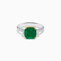 The 18K Two Tone Gold Emerald and Diamond Ring features a large square-cut green emerald in an 18K gold prong setting, with a white metal band accented by small round diamonds on each side.