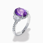 The Effy Hematian 18K White Gold Oval Purple Sapphire and Diamond Halo Ring features a central oval purple sapphire, two oval white diamonds, and smaller diamonds along the band, displayed on a white background.